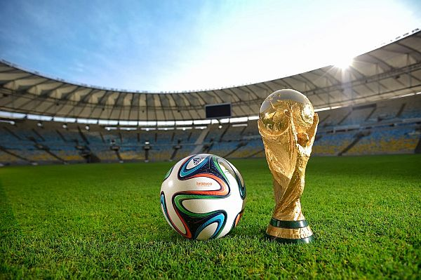 A football and the World Cup trophy on the pitch of an empty stadium at dusk.